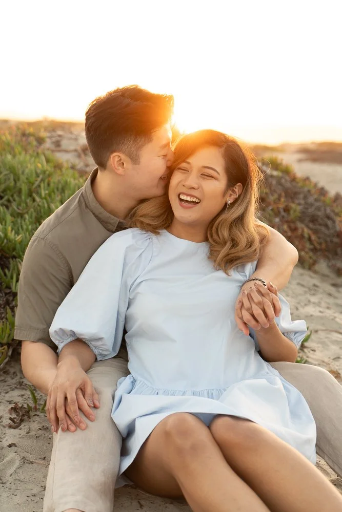 A couple sitting on the beach at sunset, embracing and smiling happily.