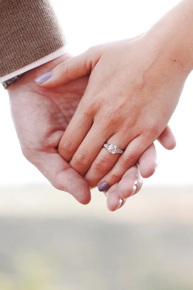 Close-up of two hands holding each other, with focus on an engagement ring on the woman's finger.