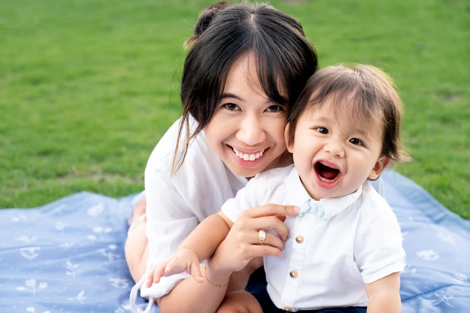 Smiling woman and laughing child lying on a blanket outdoors on grass