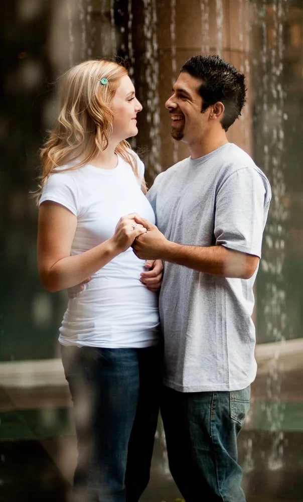 A young couple is holding hands and smiling at each other outdoors near a waterfall.
