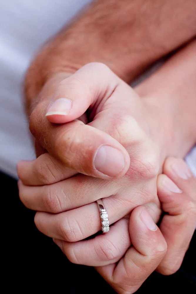 Close-up of two hands clasped together, one with an engagement ring with multiple diamonds.