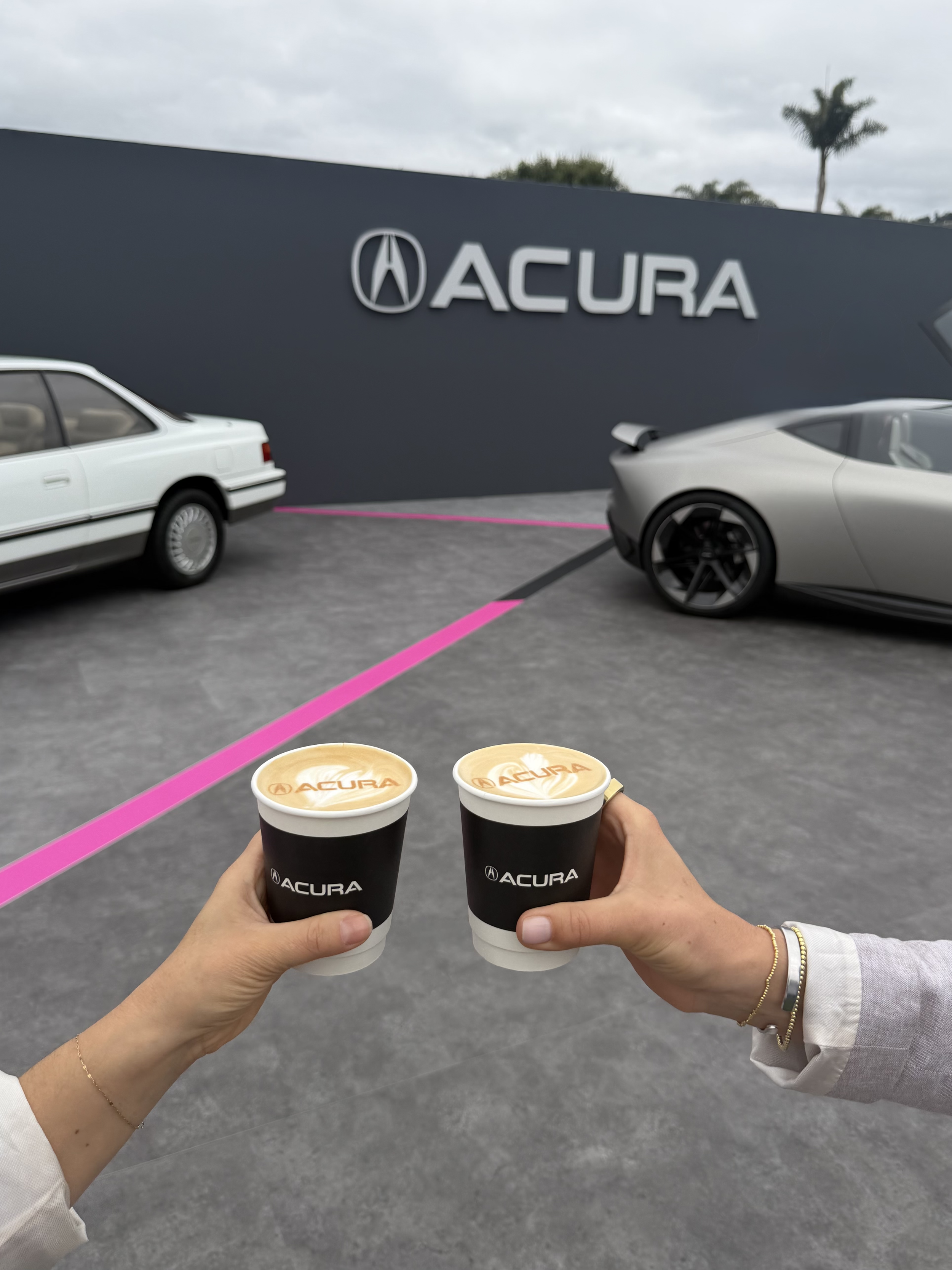 Acure branded coffee cups and latte art in front of two acura cars and an acura branded back drop