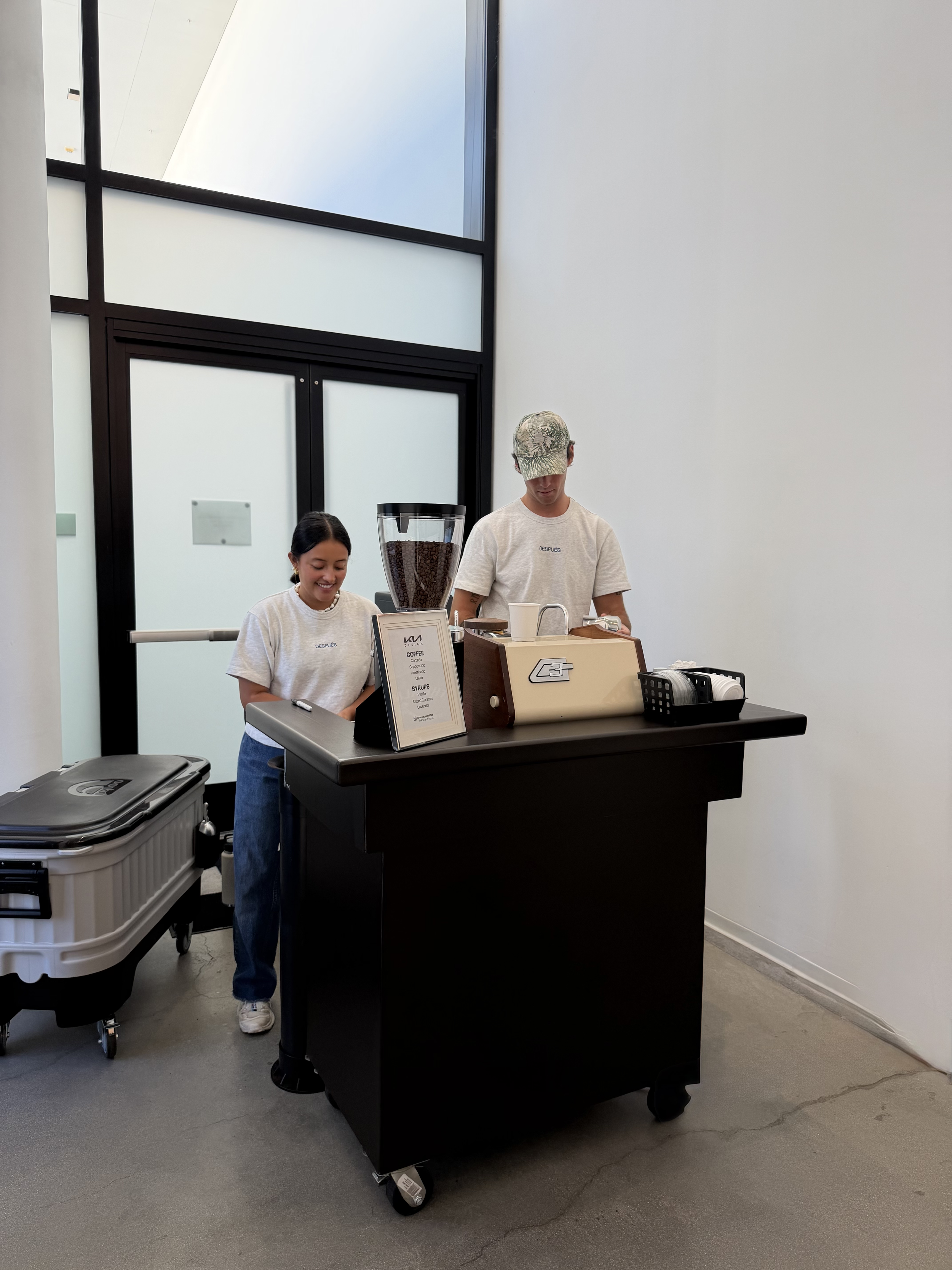 A black coffee cart with two baristas behind it is pictured with a cream colored espresso machine and a coffee cart menu.