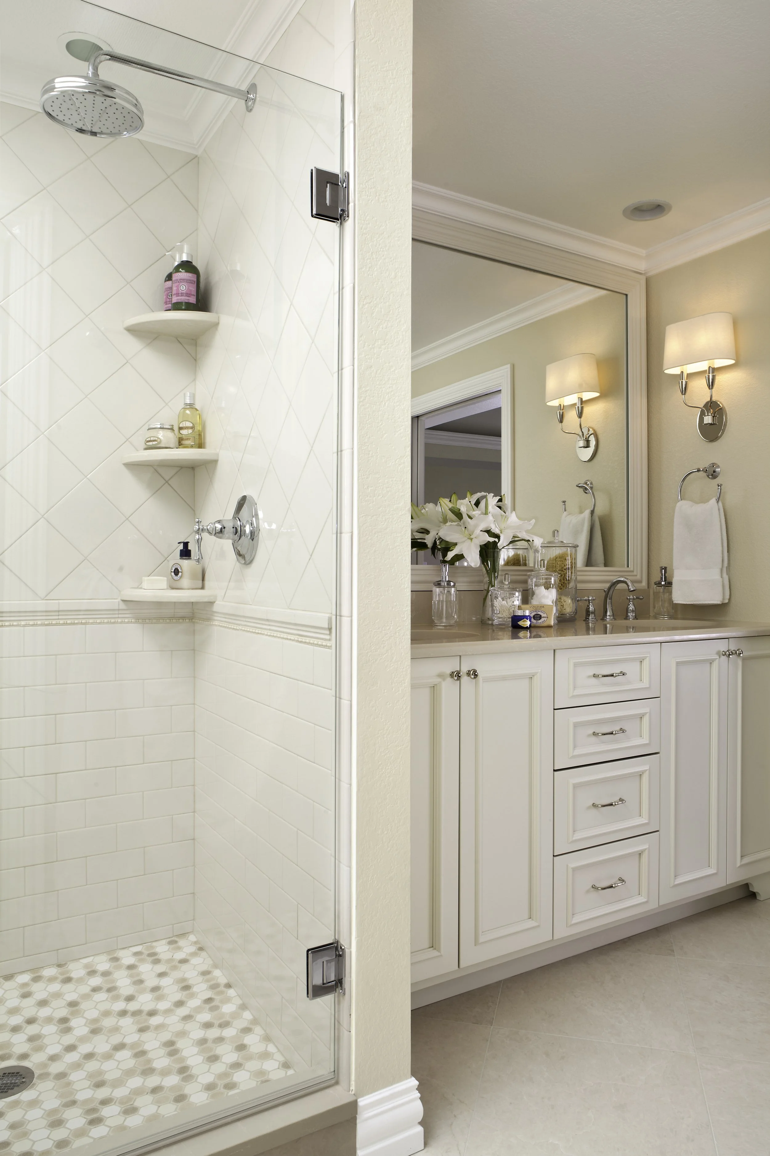 A bathroom with a walk-in shower and a vanity with a large mirror, decorated with flowers and toiletries.