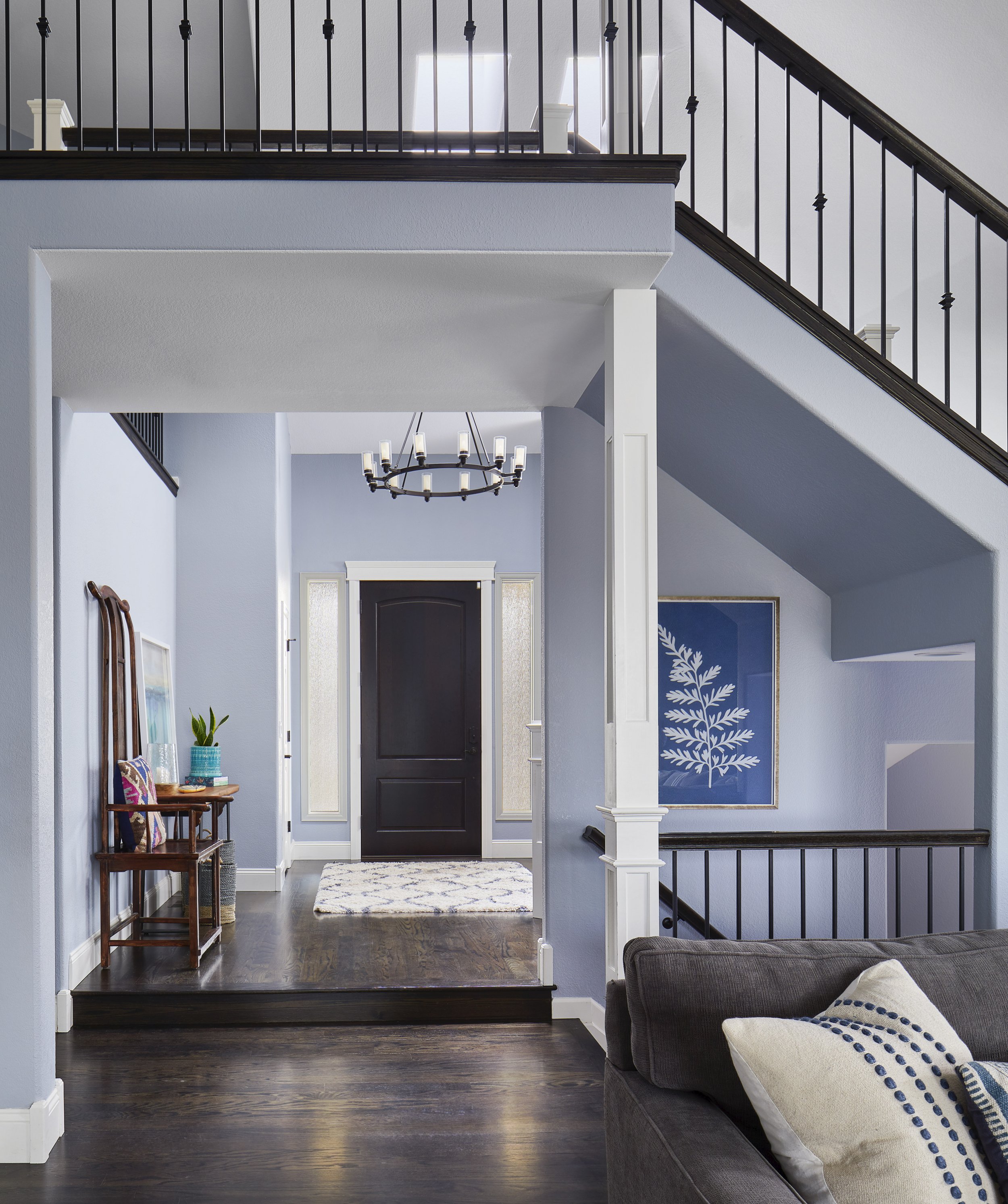 Entryway of a modern home with a dark front door, light blue walls, a chandelier, and a staircase with black railing.