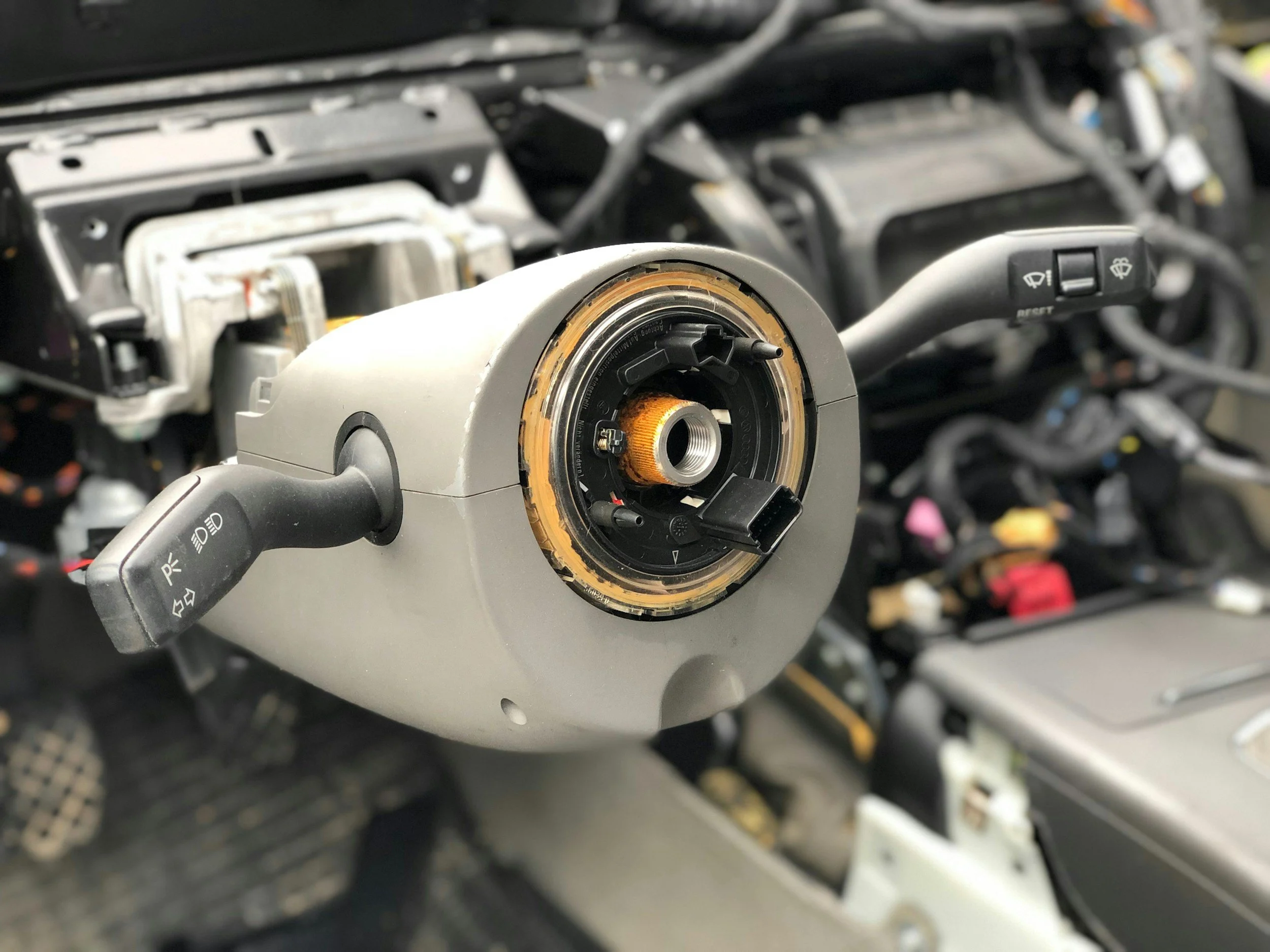 Close-up of a disassembled car steering column with internal components visible, including stalk controls on either side.