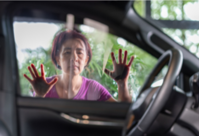 A woman looking through a car window with her hands pressed against the glass, outside the vehicle.