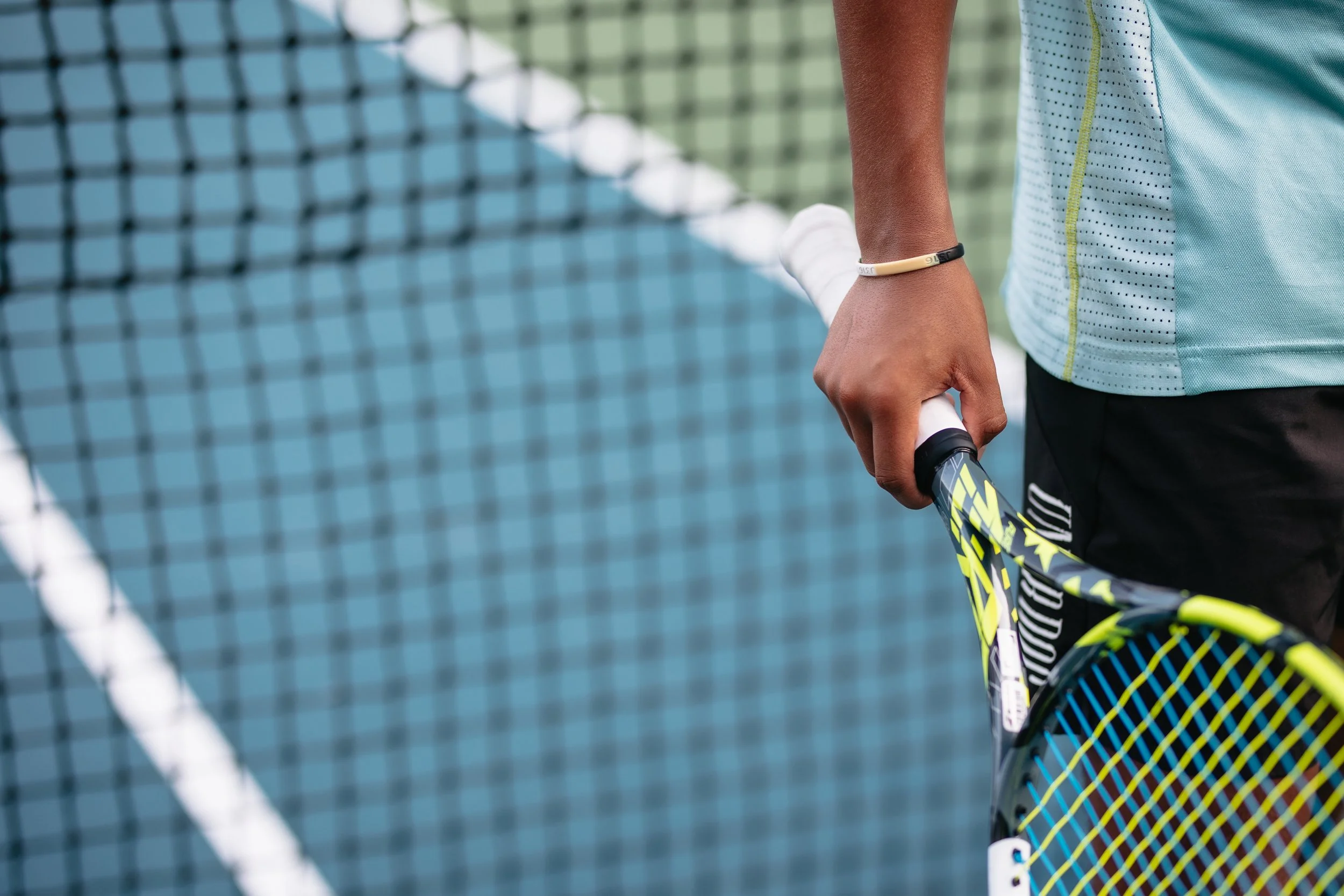A close-up of a person holding a tennis racket on a tennis court with a net in the background.