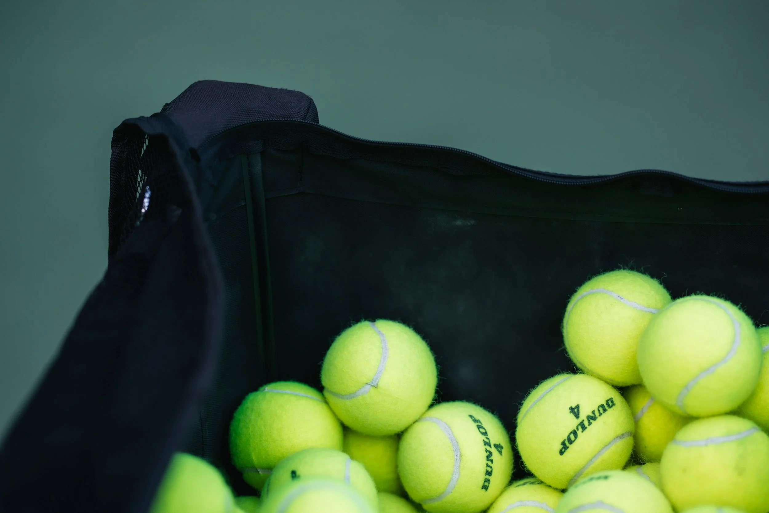 Open black tennis bag filled with bright yellow tennis balls.