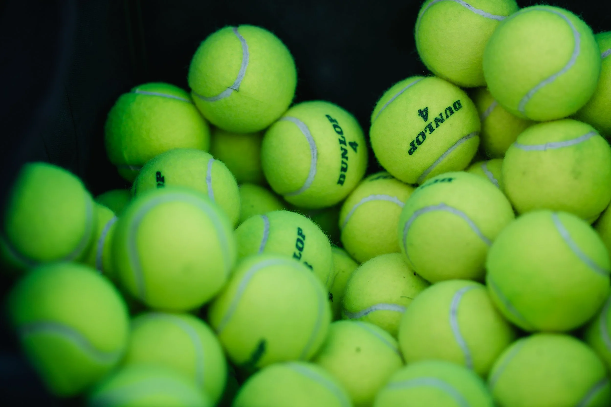 A collection of bright yellow tennis balls, some with black text, piled together.