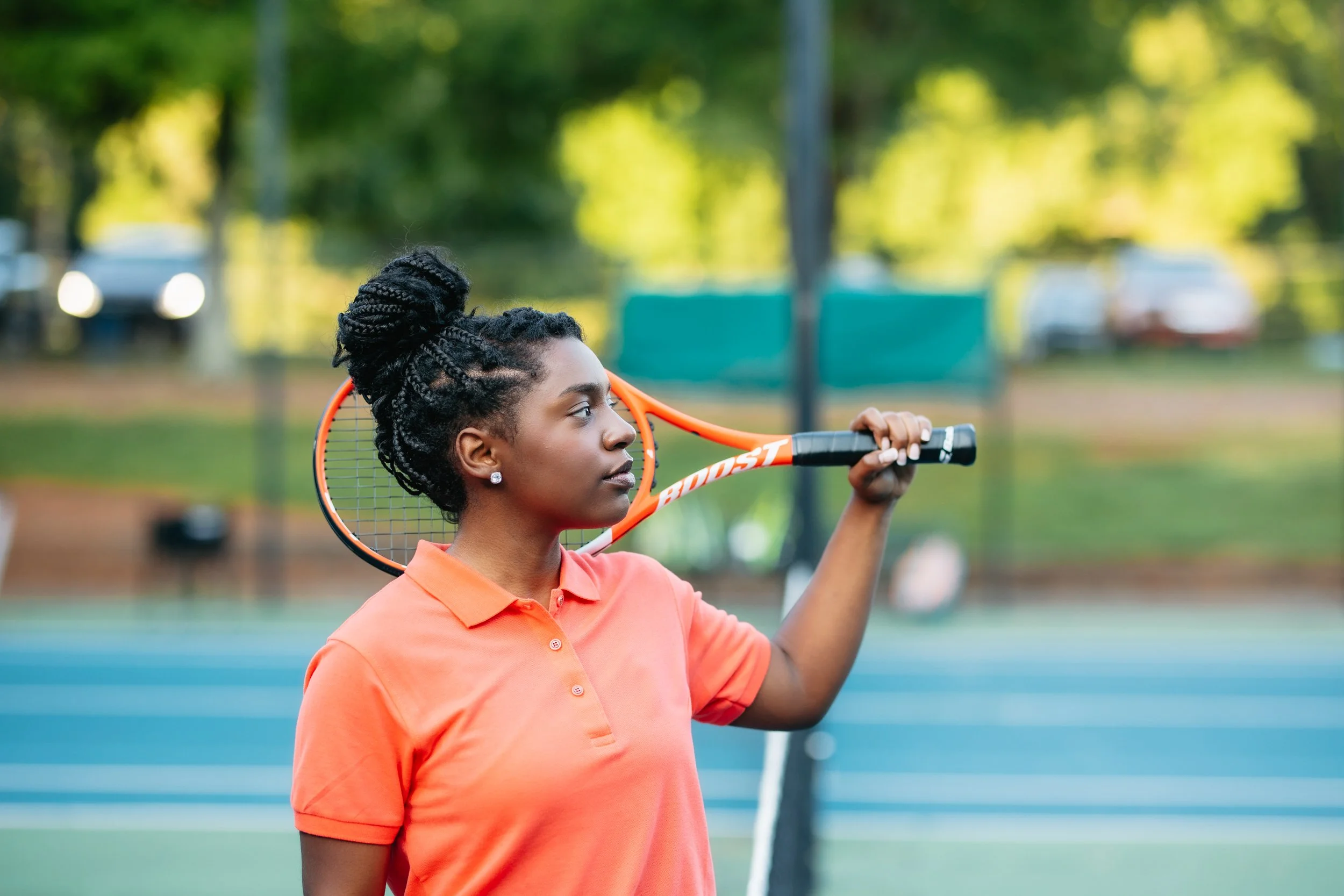 A woman in an orange polo shirt holding a tennis racket on a tennis court outdoors