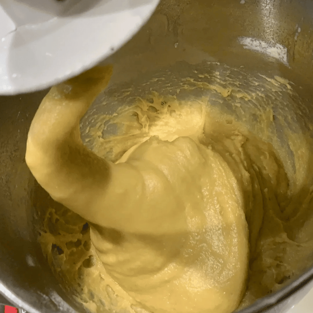 Close-up of yellow dough or batter being mixed in a metal mixing bowl.