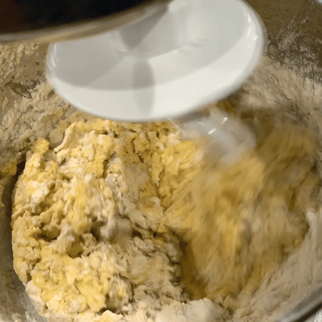 Flour and eggs in a mixing bowl, with a spoon pouring liquid into the mixture.