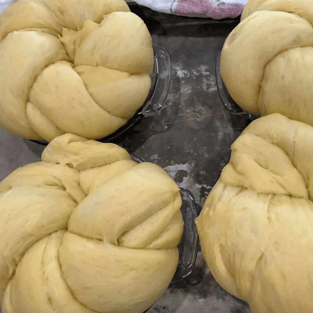 Four bowls of braided bread dough on a dark countertop.