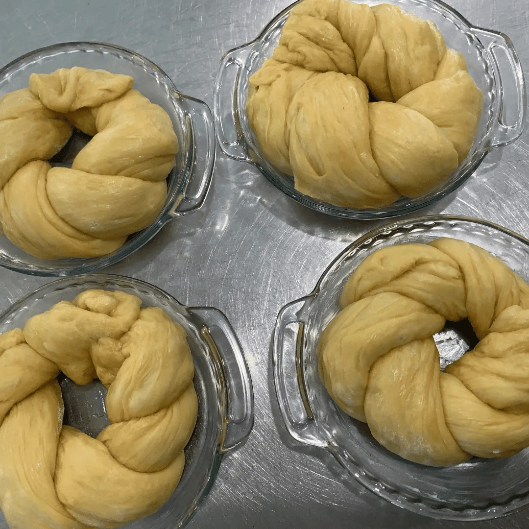 Four glass bowls filled with uncooked croissants or pastry dough on a metallic surface.