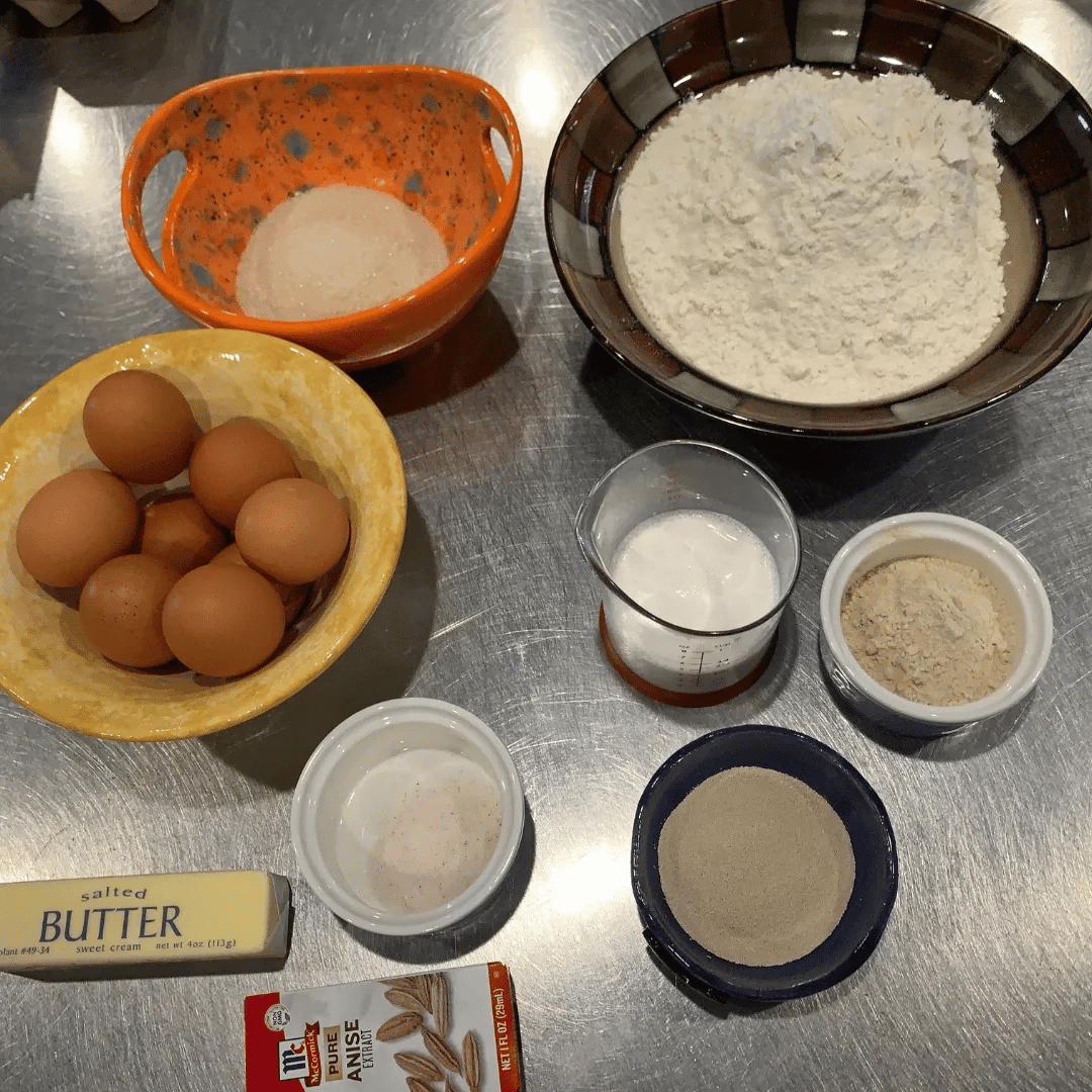 Baking ingredients including eggs, flour, sugar, milk, butter, and various seasonings on a metal surface.