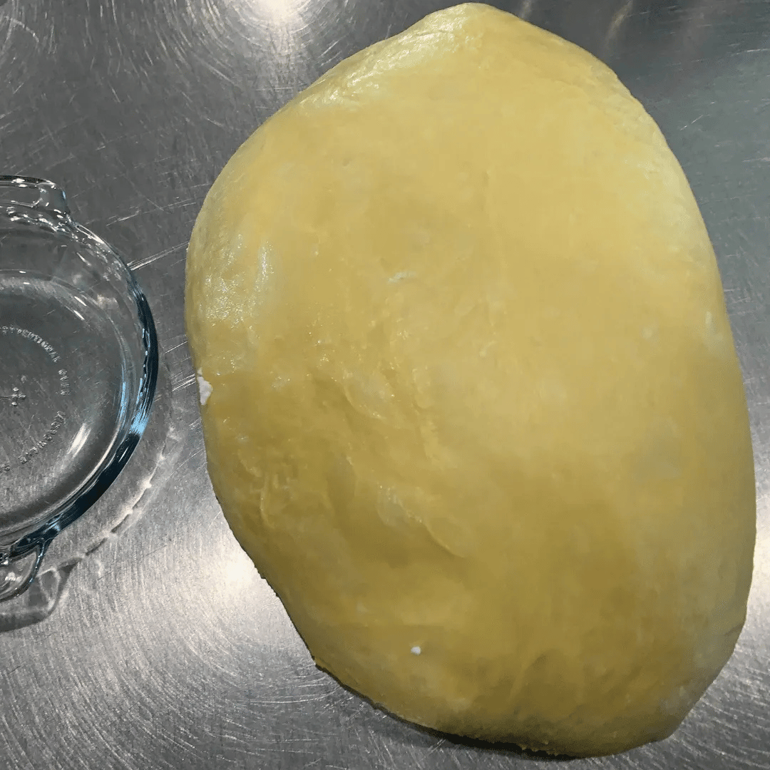 Uncooked yellow potato on a metal surface, with a glass bowl nearby.