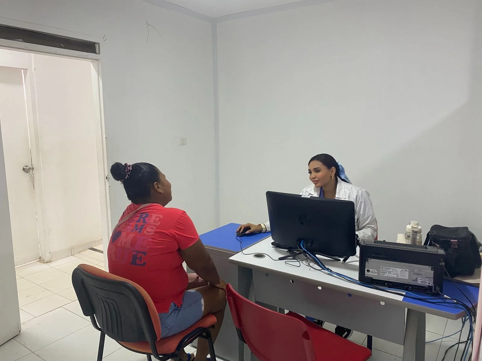 Una mujer en consulta médica con una doctora en una clínica, sentadas frente a frente en una oficina sencilla y moderna.