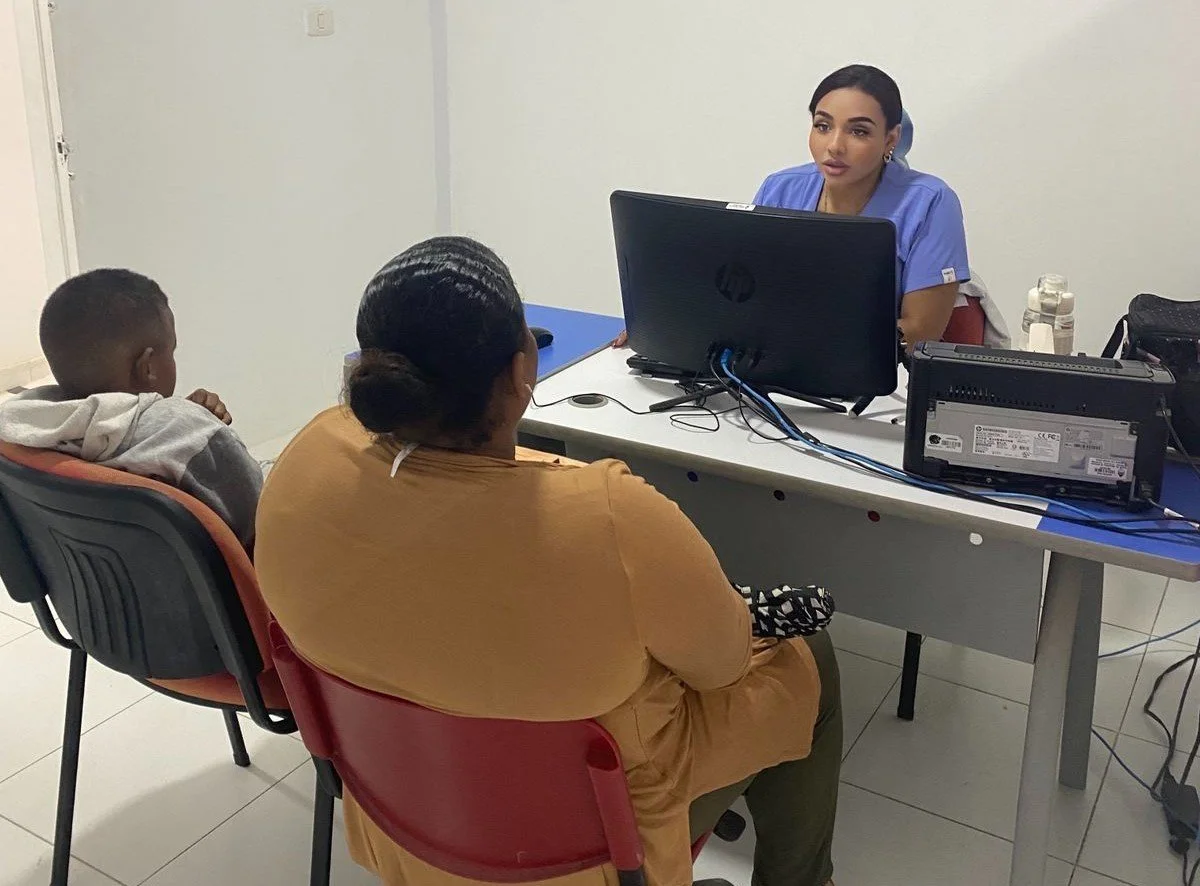 Una mujer y un niño sentados frente a una recepcionista en una oficina, atendiendo una consulta.