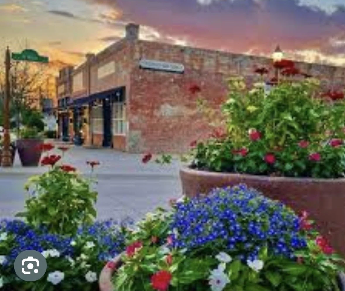 Colorful flower pots with red, white, and blue flowers in front of a brick building during sunset.