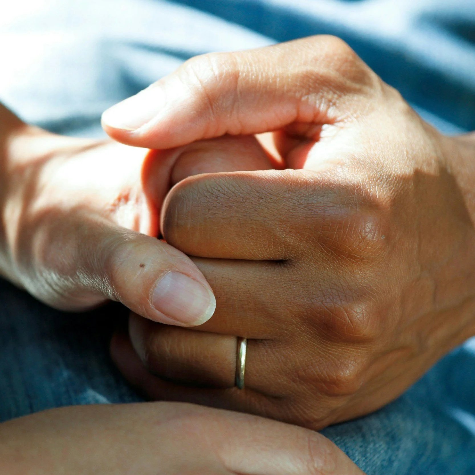 Close-up of two hands gently holding each other, one hand with a ring on the ring finger.