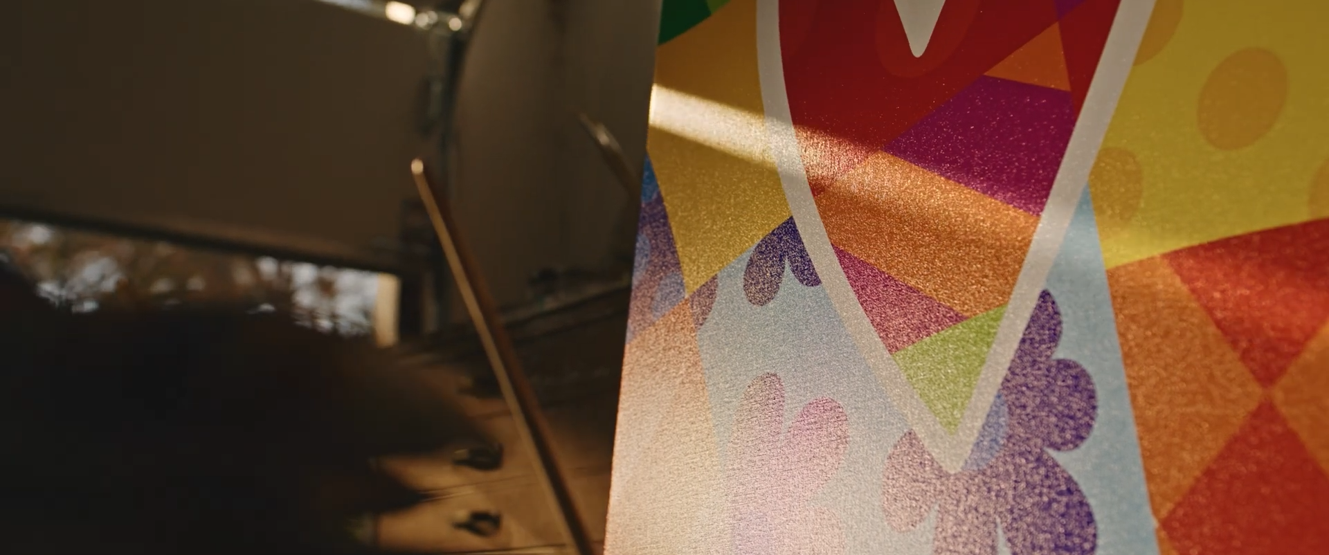 A colorful piece of artwork or poster featuring geometric shapes and patterns, partially illuminated, with a blurred background.