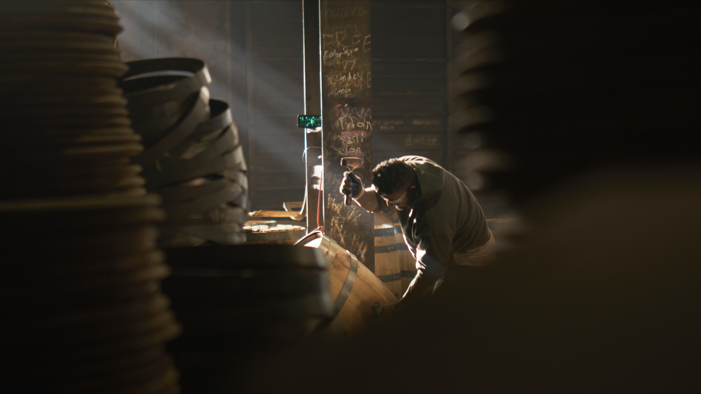 A person working with a tool in a dimly lit space with sunlight streaming in, surrounded by stacked plates.