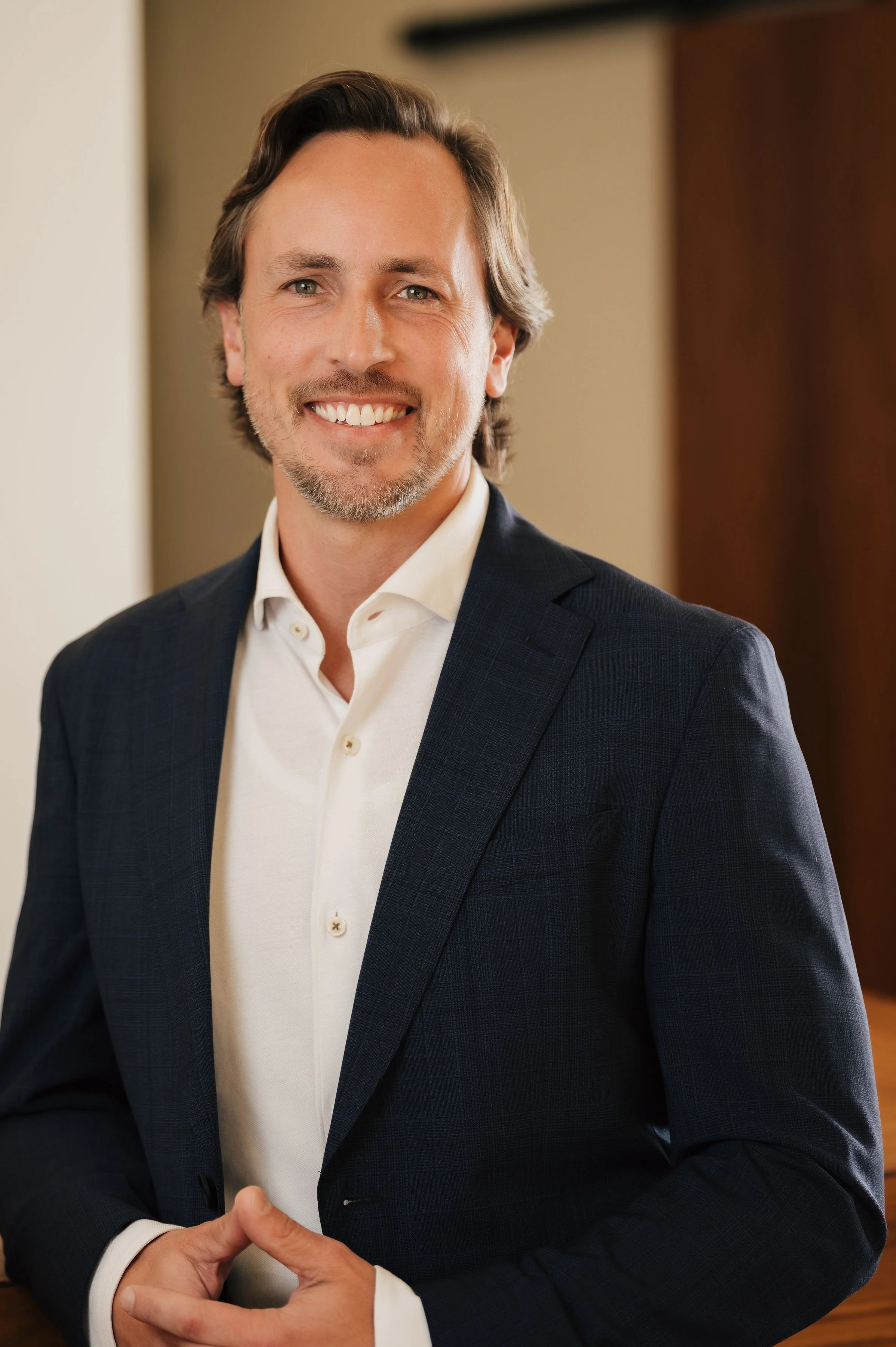 Professional man in a dark blazer and white shirt standing indoors.