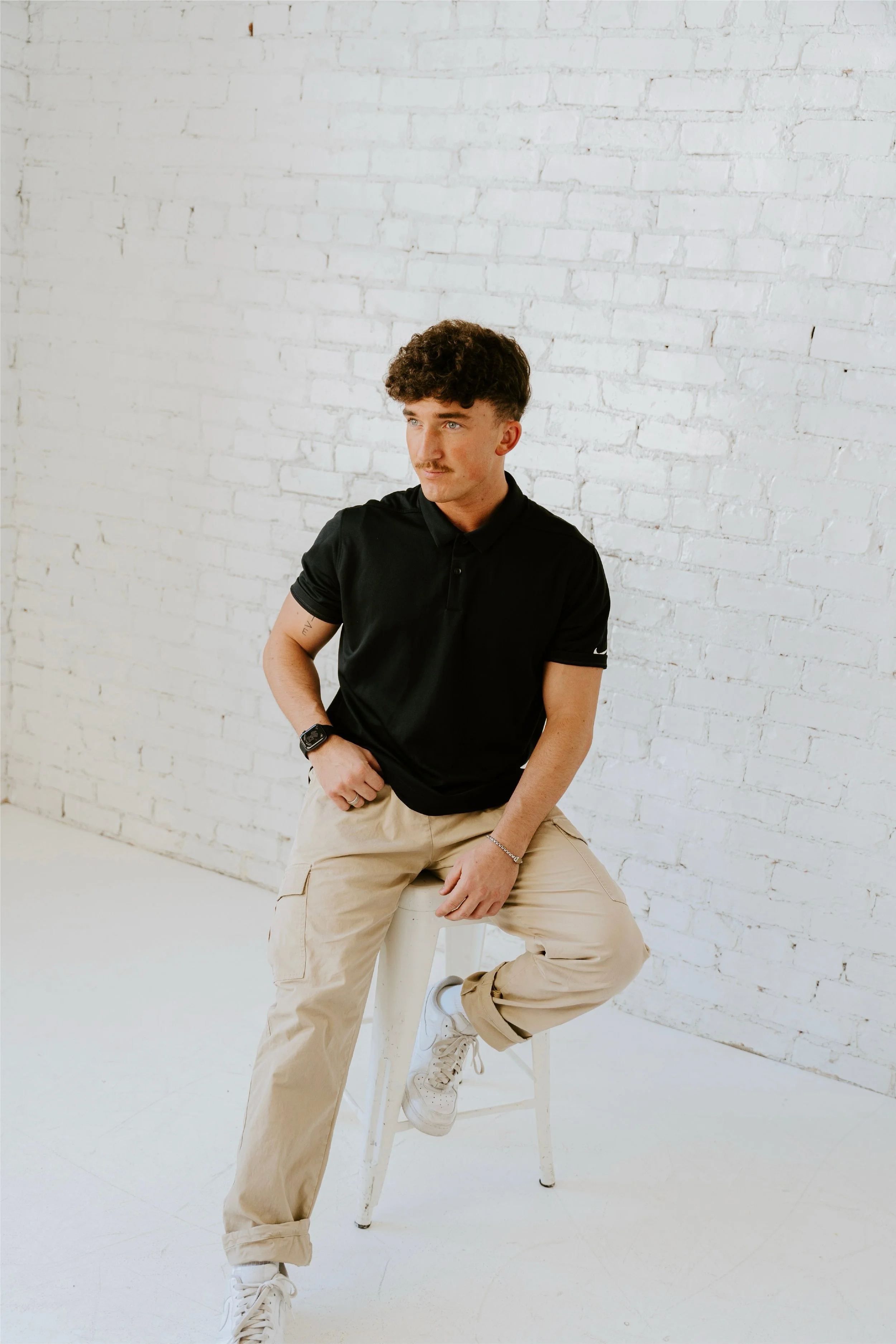 Portrait of a young man seated against a white brick wall.