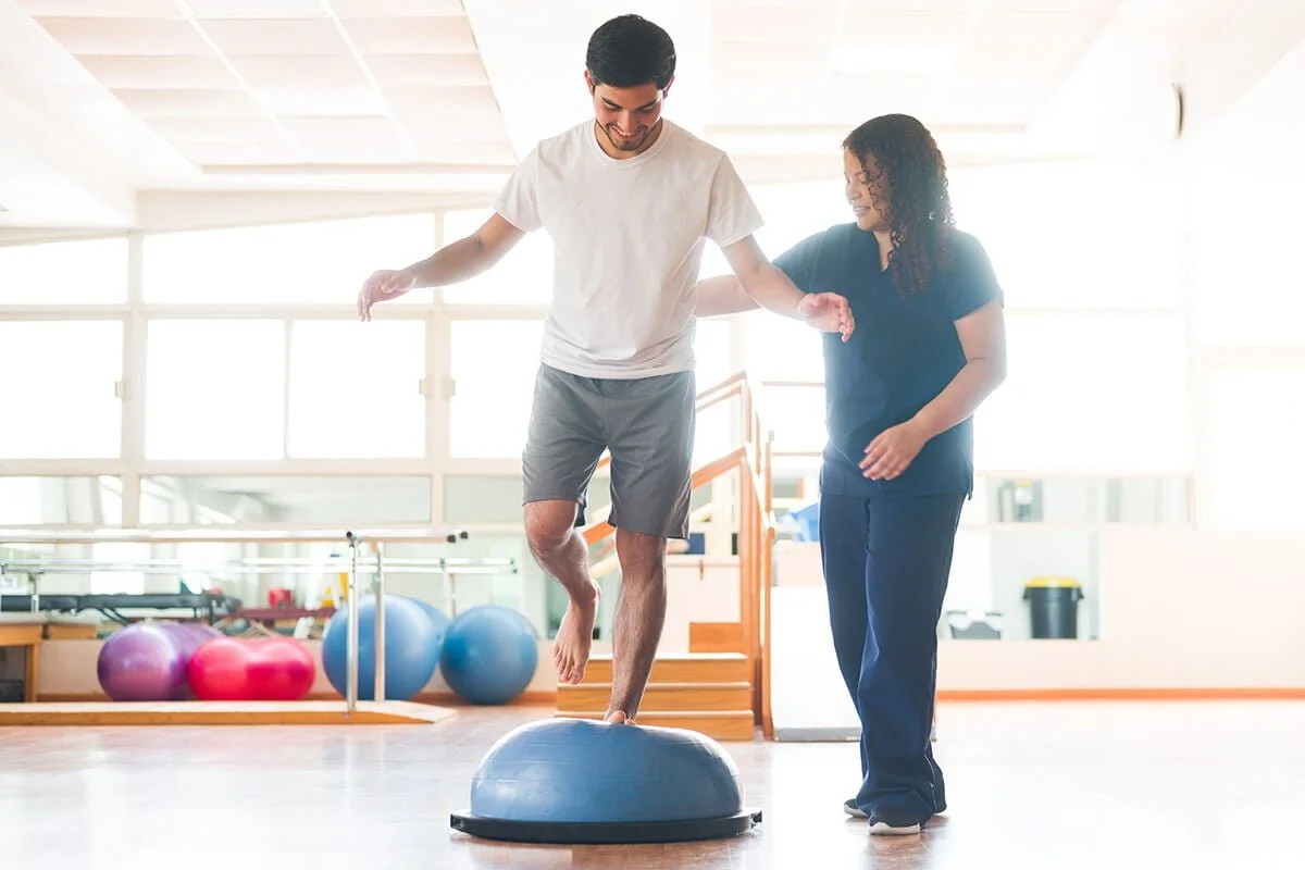 Man standing on bosu ball assisted by therapist