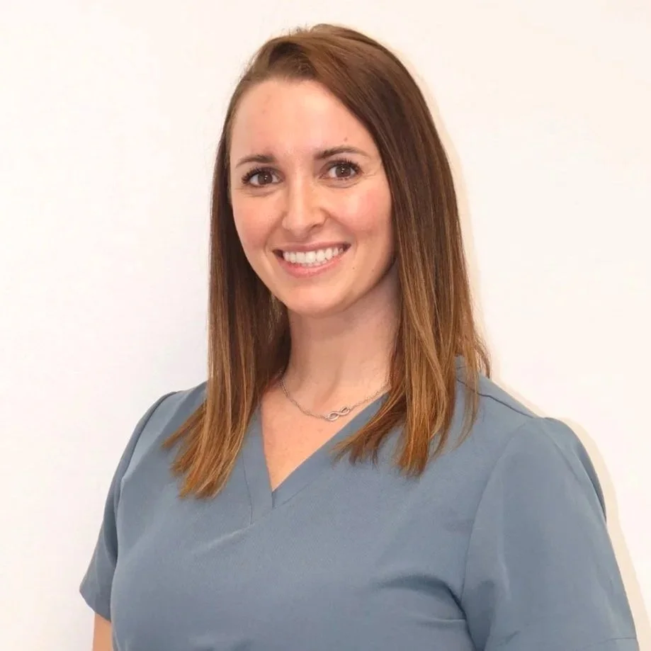 A woman smiling at the camera holding a test strip, wearing blue gloves, with a colorful abstract painting in the background.