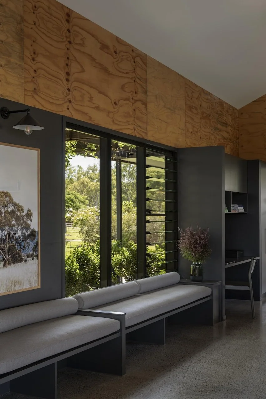Interior of a modern room with black framed windows, a long gray cushioned bench, a potted plant, and wooden wall paneling.