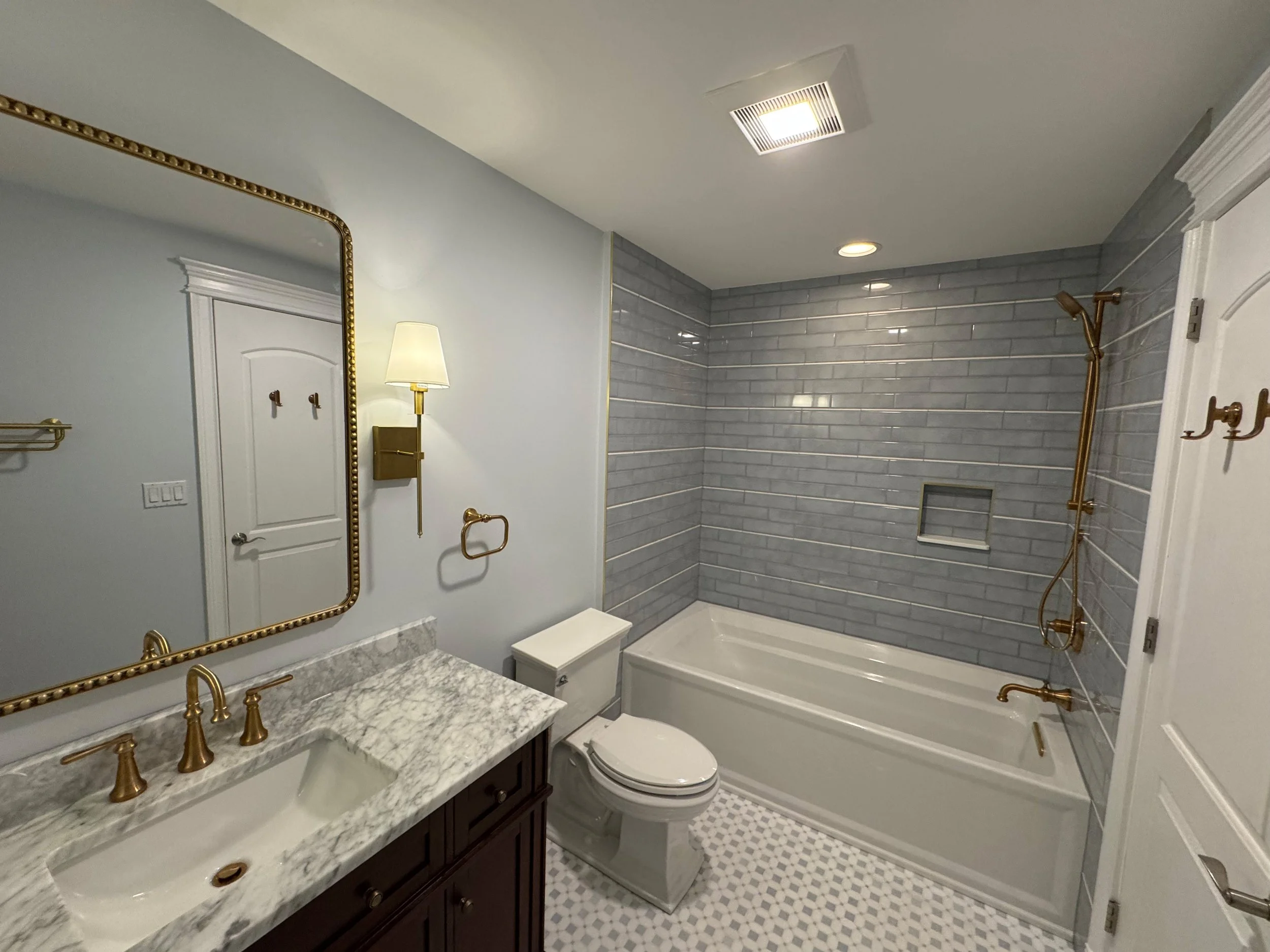 Bathroom with gray tiled shower, white tub, marble vanity, and gold fixtures.