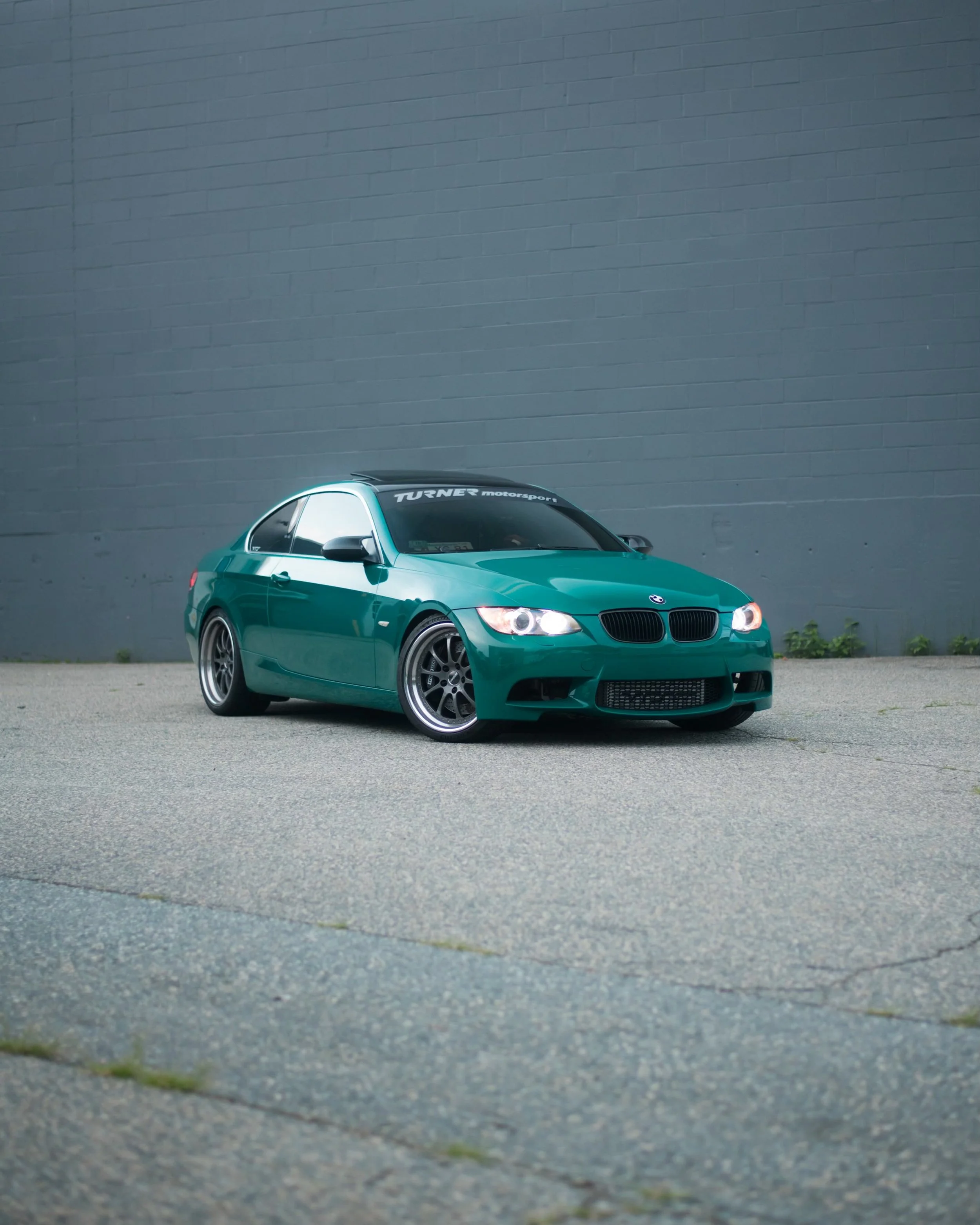 A green BMW car parked on pavement in front of a gray wall.