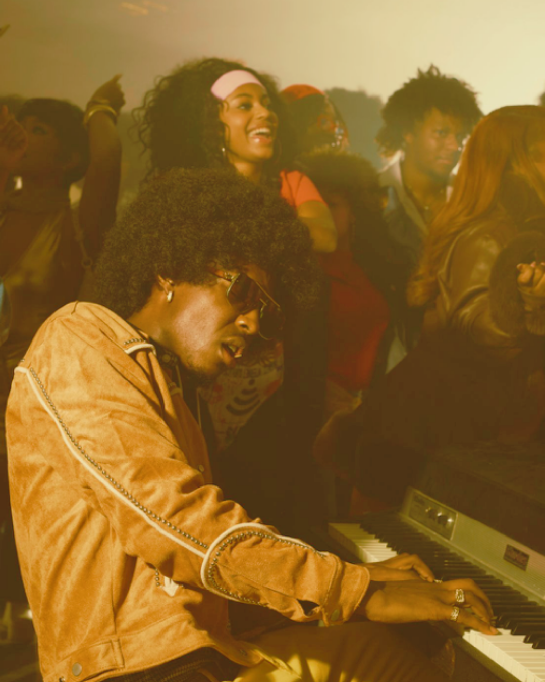 A man playing a keyboard at a lively party with a woman smiling and dancing in the background.