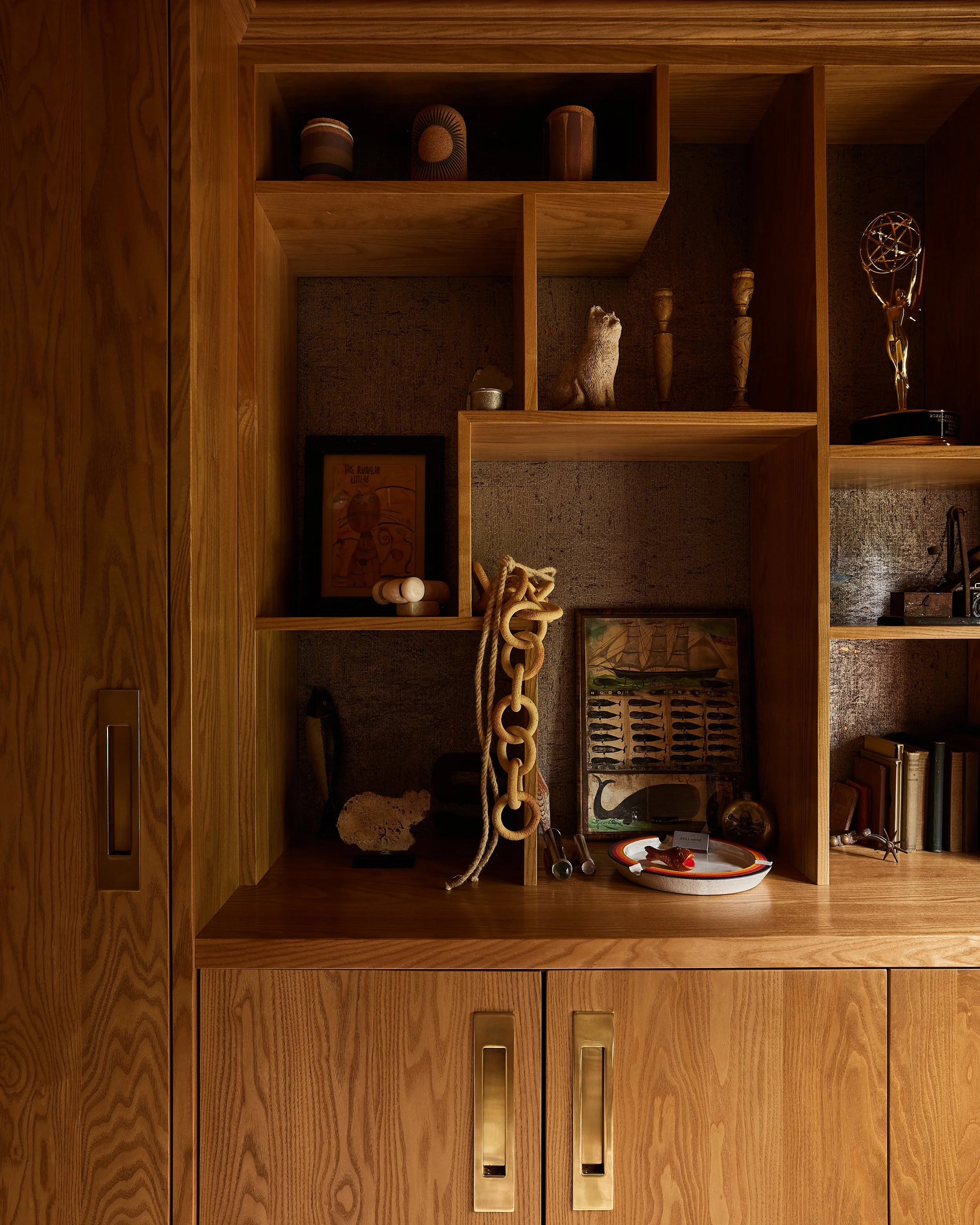 A wooden display cabinet with various decorative items including vases, artwork, a toy chain, a sculpture, and books.