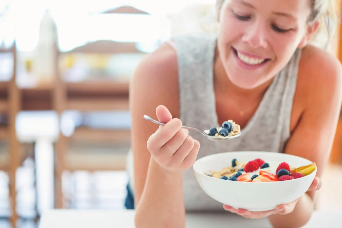 woman smiling while standing at bench eating bowl of muesli an example of a healthy meal while on GLP-1
