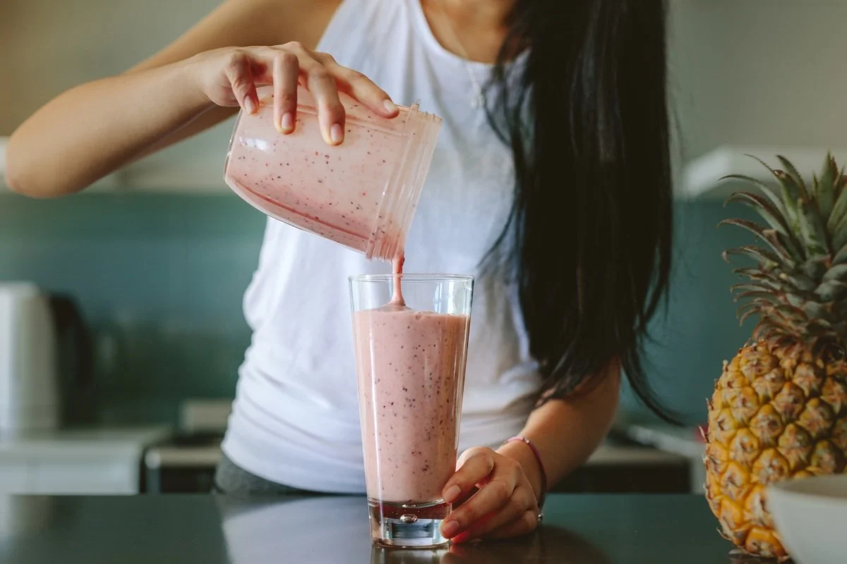 A person pouring a pink smoothie from a blender cup into a tall glass as part of a semaglutide diet plan