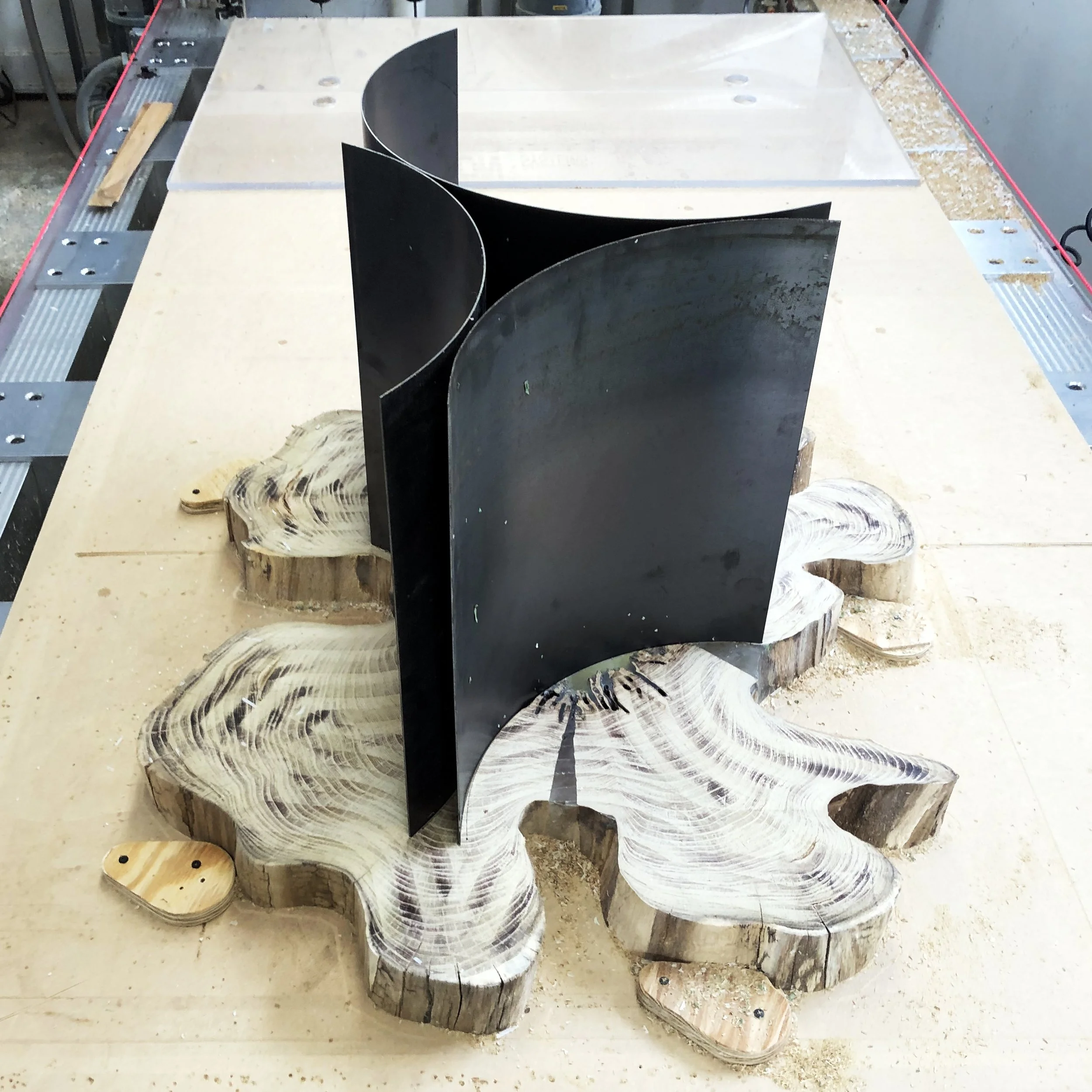 A wood sculpture with a black metal divider in the center, placed on a wooden slab with natural edges, on a workbench in a woodworking shop.