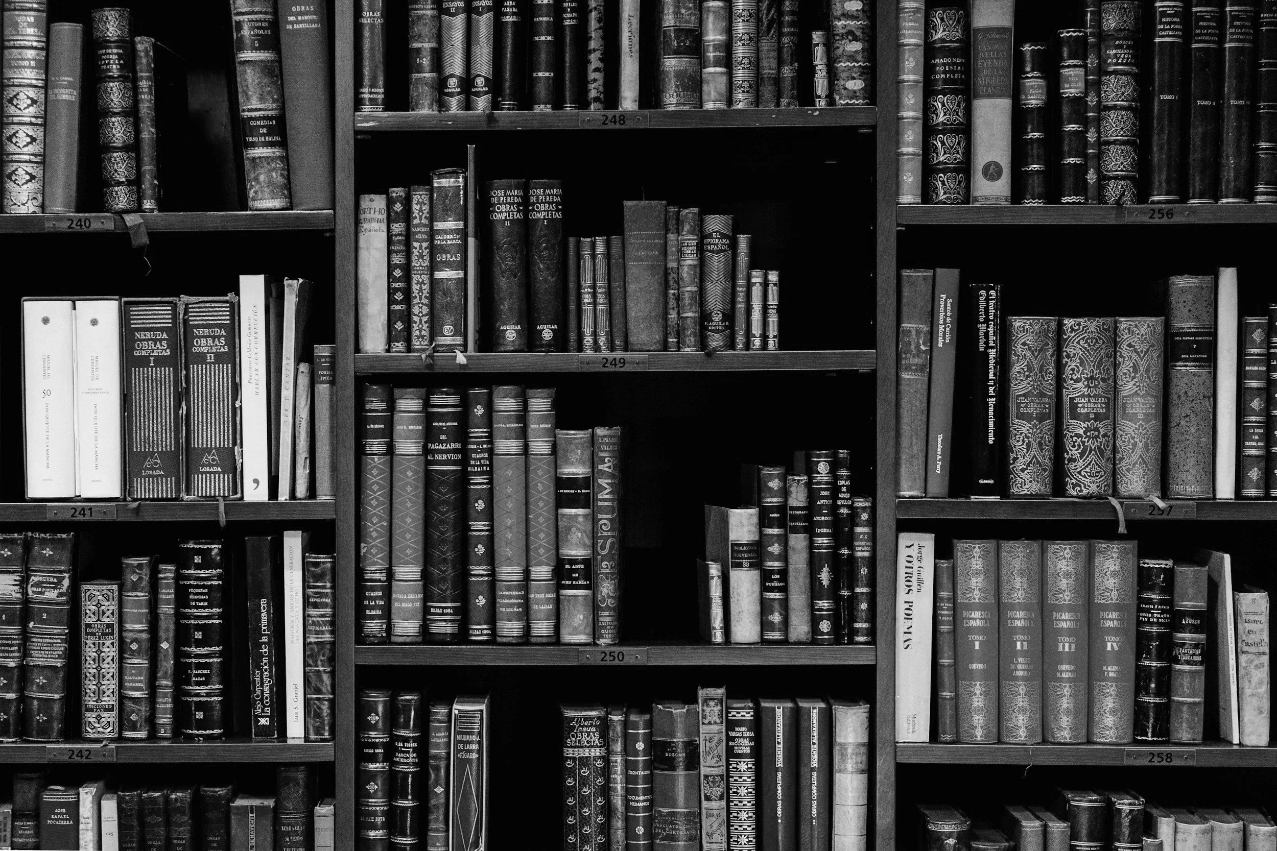 Black and white image of wooden bookshelves filled with many books of various sizes and designs.