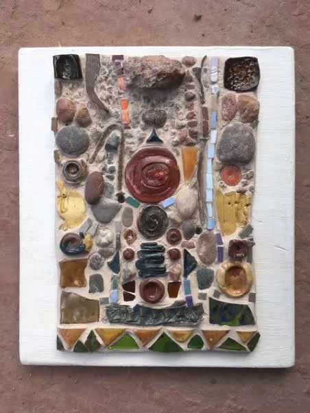 Artwork made of various stones, broken tiles, and other small objects arranged on a white rectangular board.
