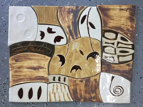 A hand-painted ceramic tile mural with abstract shapes and patterns in earth tones like brown, beige, and white.