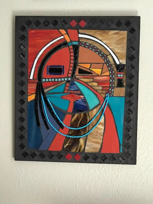 Abstract colorful artwork with geometric shapes and patterns, framed in black, hanging on a white wall.