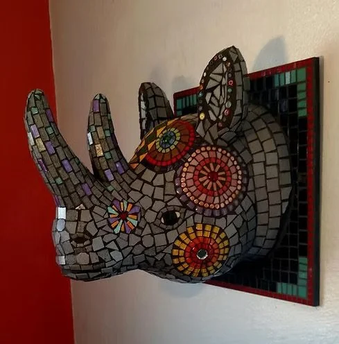 Mosaic art sculpture of a rhinoceros head with colorful patterns, mounted on a wall.