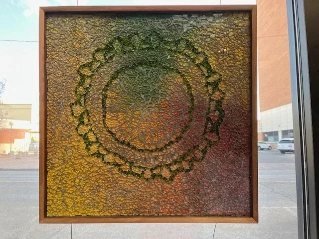 Abstract textured artwork with a circular pattern in the center, framed with wood, hanging on a wall.