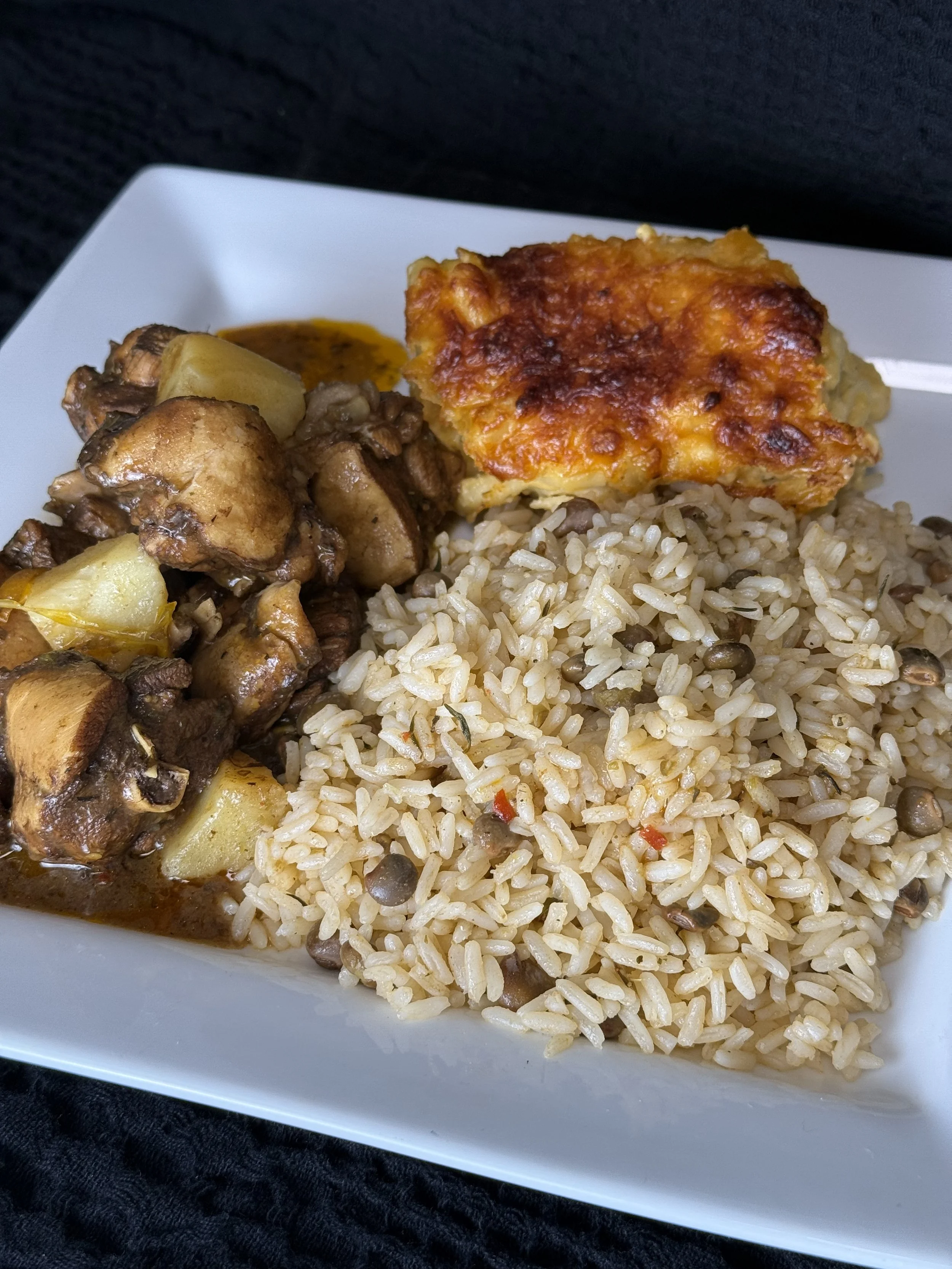 Plate of baked chicken with tomato sauce, seasoned rice with lentils, and beef stew with potatoes on a white square plate.
