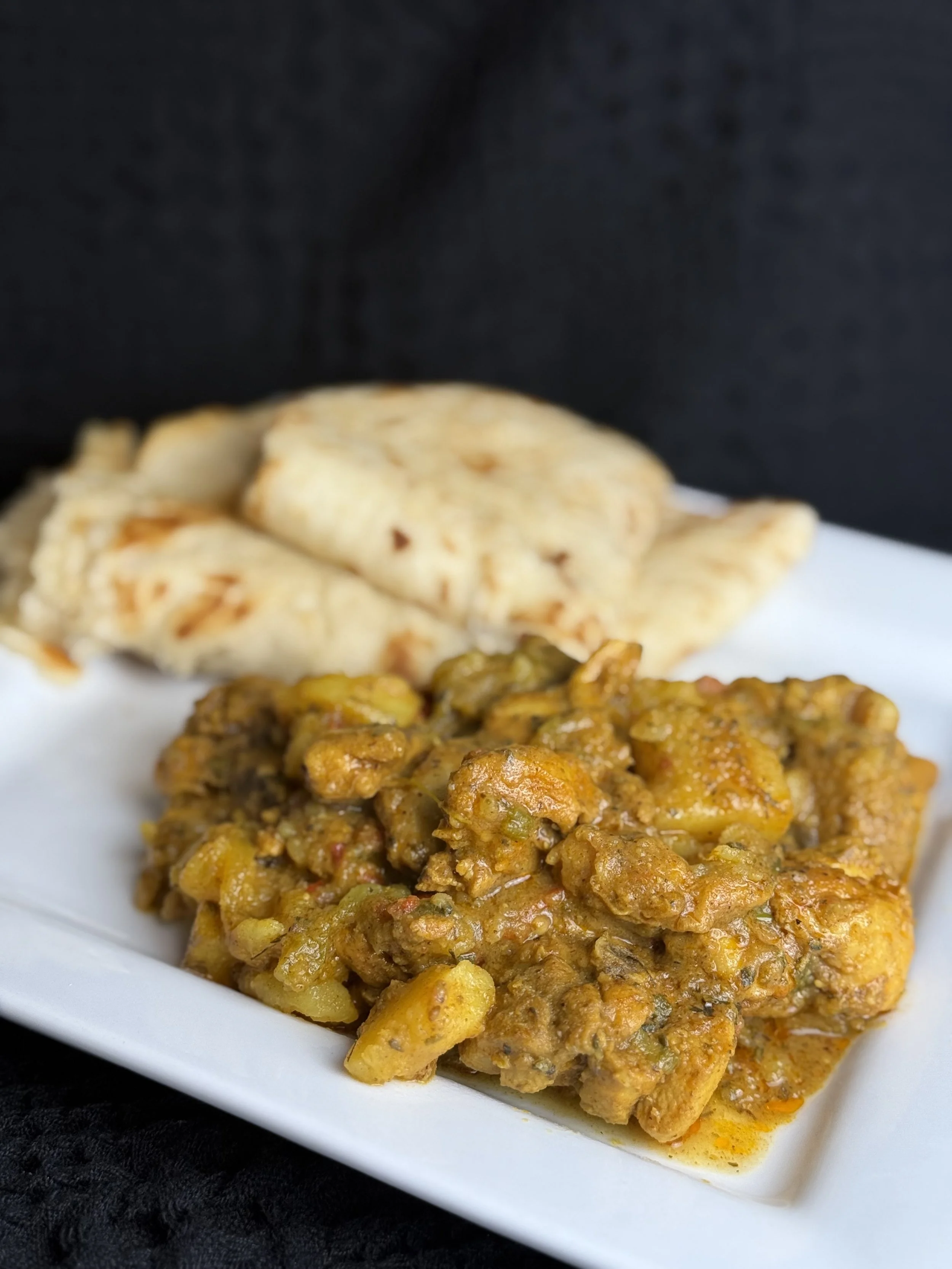 Indian dish with curry, potatoes, and spices served with flatbread on a white plate