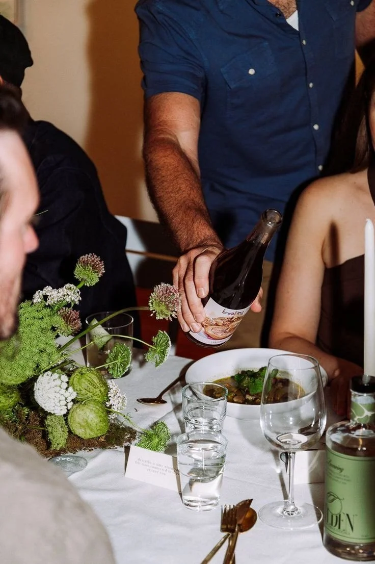 Person pouring a beverage at a dinner table with flowers and glassware