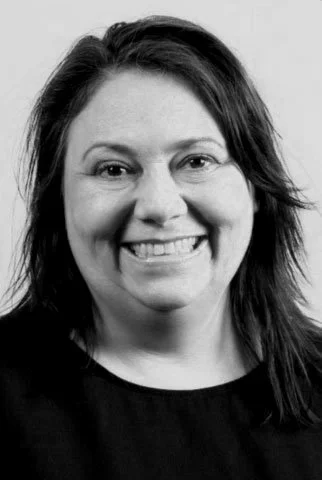 Black and white portrait of Tamara Giles with shoulder-length hair, wearing a dark top.