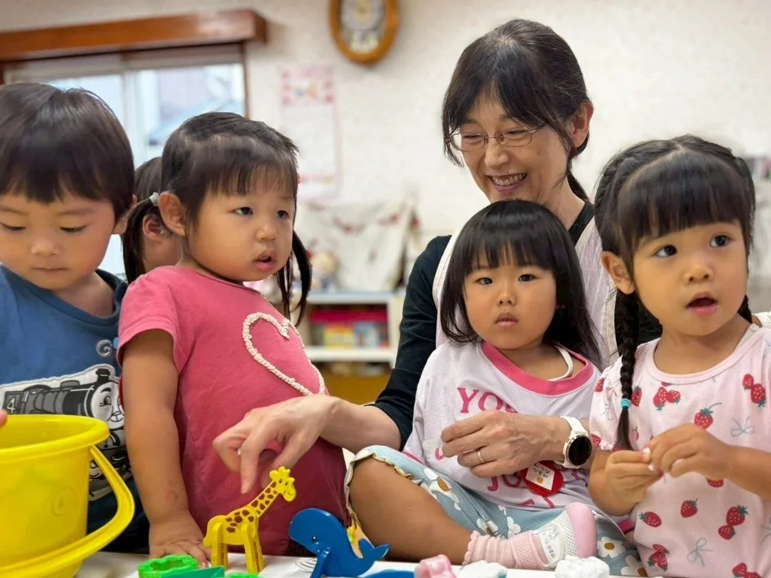 幼稚園の教室で教師と子供たちが遊んでいる。